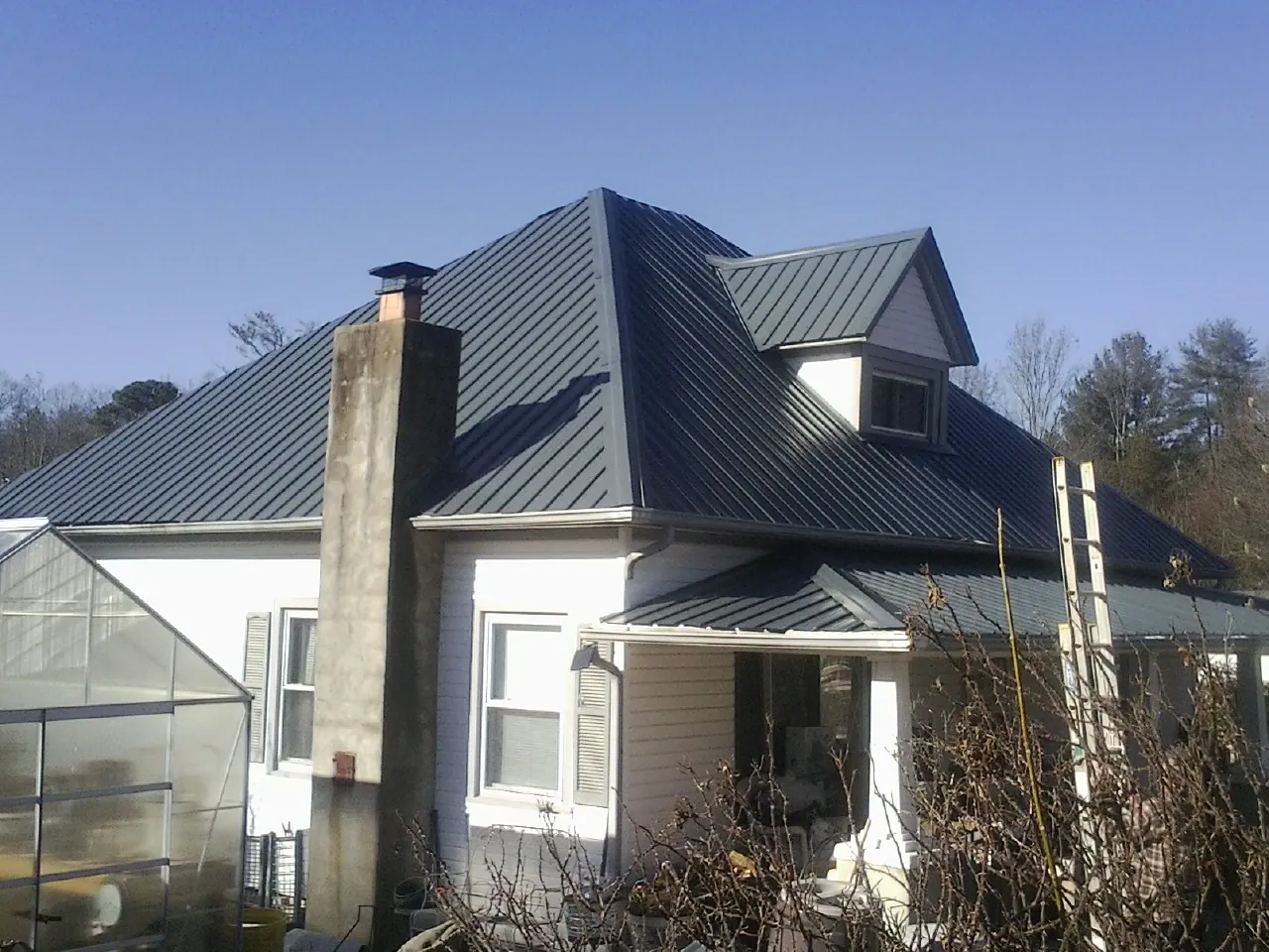 Dark blue standing seam metal roof on a white farmhouse with dormer — Slate & Tile Roof Repair by Roofing Brothers in Spotswood