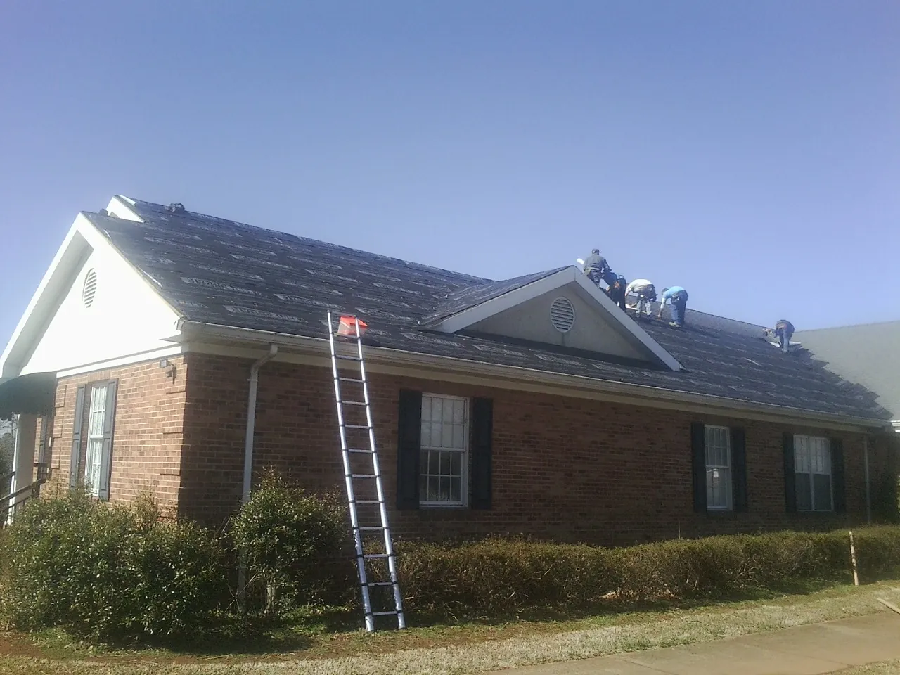 Crew tearing shingles off a brick ranch roof with a ladder set — Emergency Roof Repair work by our crew in Spotswood