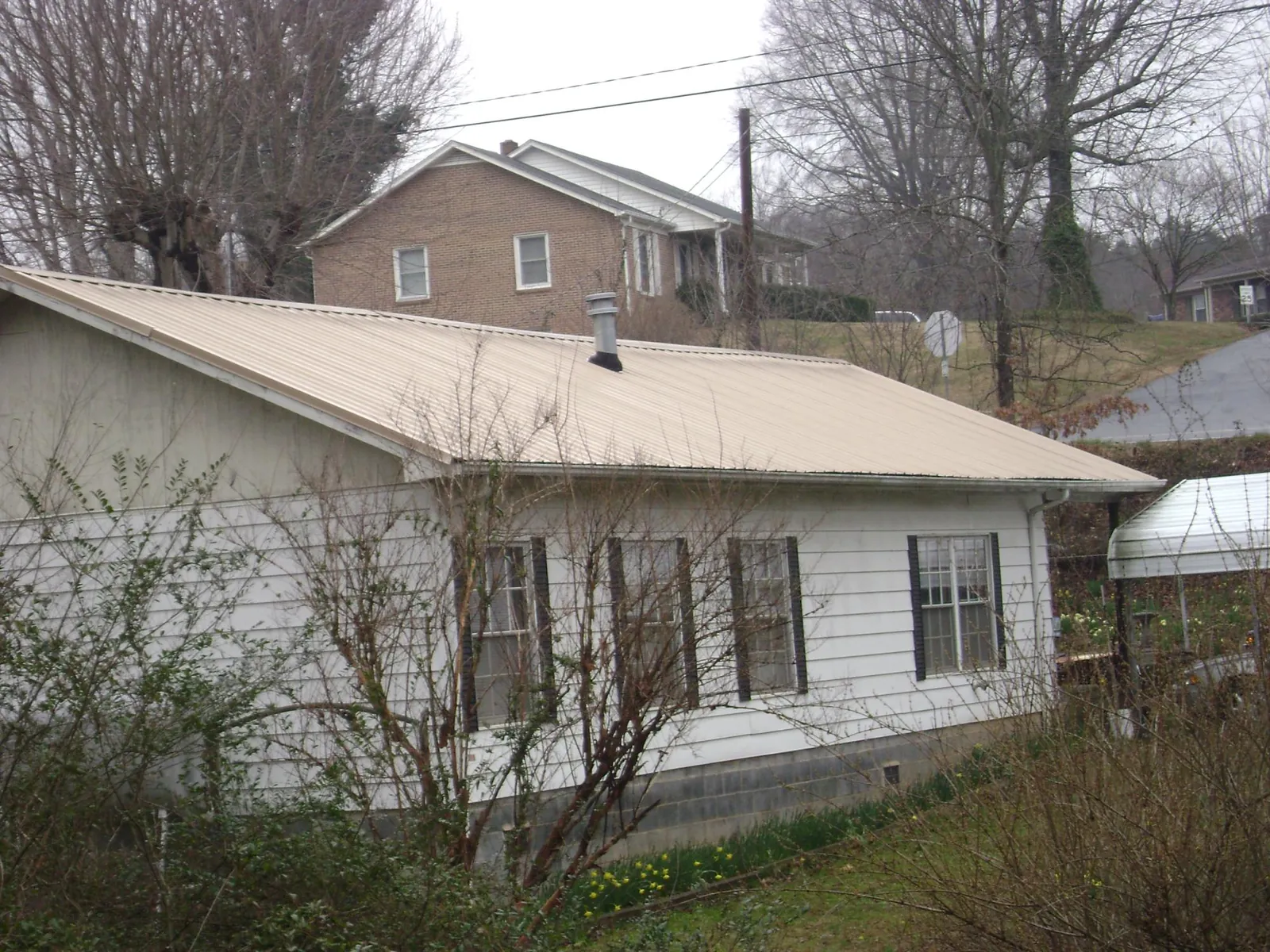 Tan metal roof on a white sided house set into a hillside — Commercial Roofing by Roofing Brothers in Spotswood